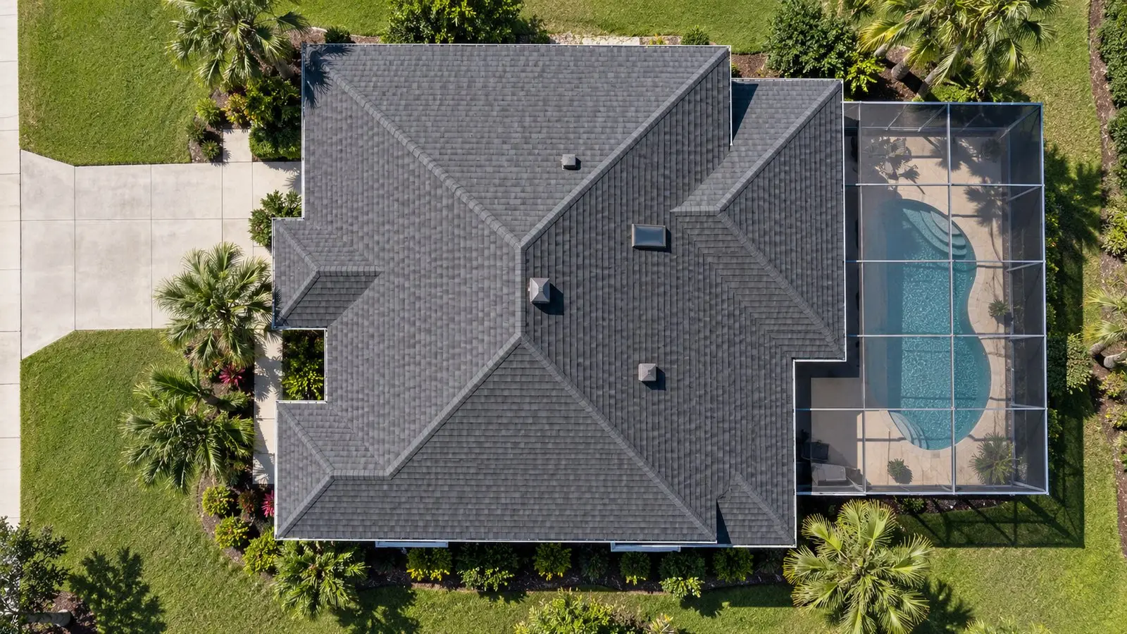 Straight-down aerial view of the shingle hip roof of a Florida home, driveway, lawn and pool enclosure