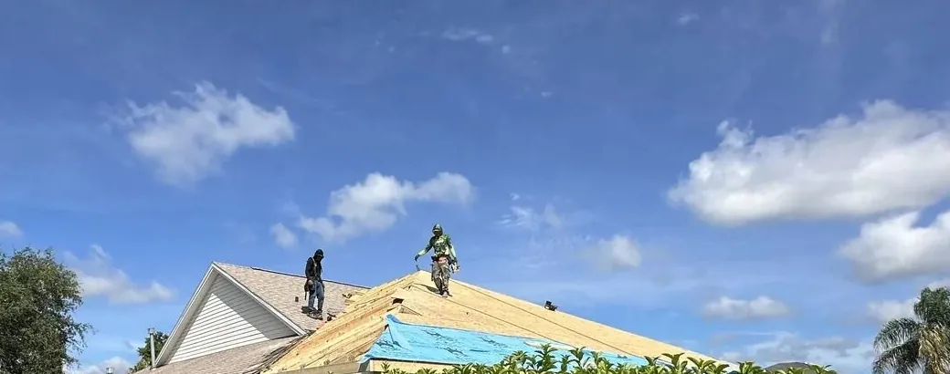 Two roofers on fresh OSB roof sheathing with blue underlayment going on at the eave, The Villages, Florida